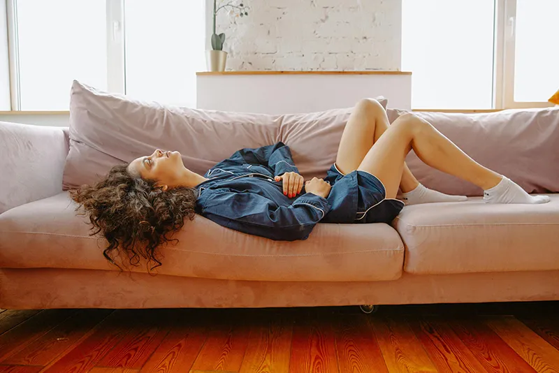 donna stesa sul divano che si massaggia la pancia in preda ai crampi addominali