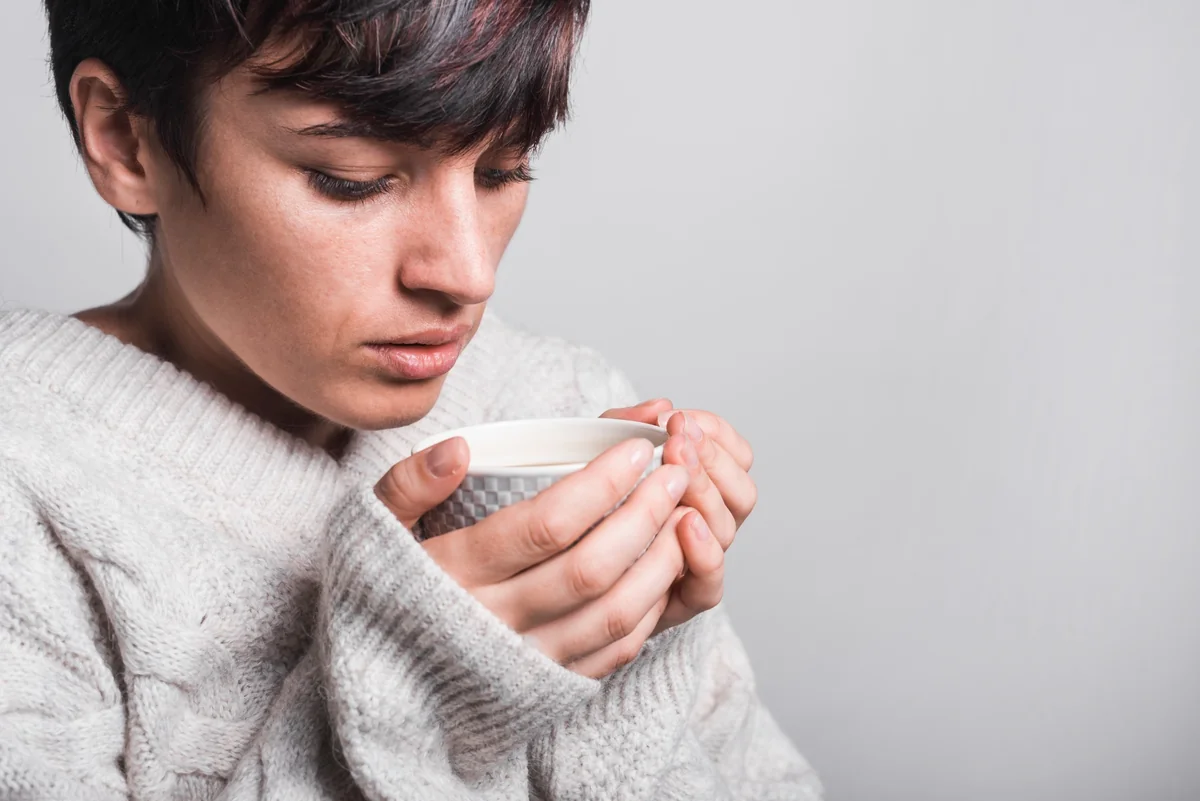 donna con capelli corti castani che tiene tra le mani tazza di tisana fumante